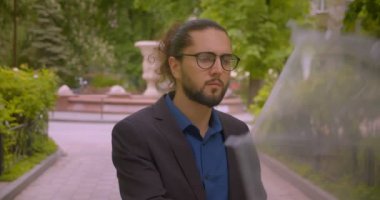 Şemsiye altında Yakışıklı hipster işadamı dikkatle etrafına bakar ve parkta memnuniyeti ile kameraya gülümsüyor.