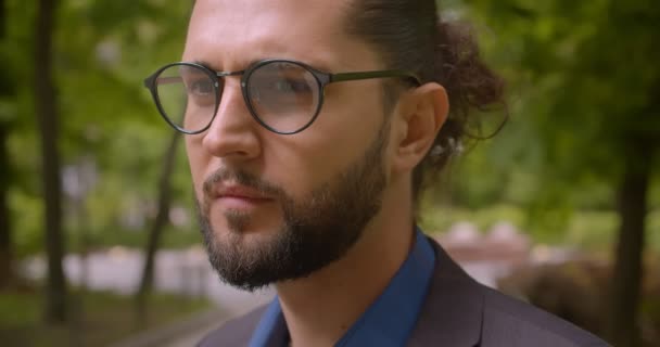 Close-up shot of handsome hipster guy in formal suit with ponytail smiling and flirting into camera in park. — Stock Video