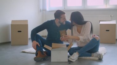 Yeni evin zemininde oturan genç beyaz çift, mutlu ve heyecanlı fotoğraflar unboxing.