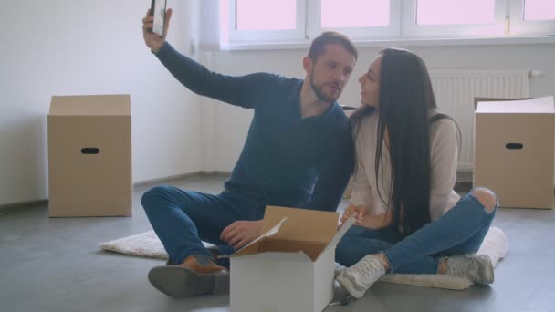 Joven pareja caucásica sentada en el suelo de la nueva casa eligiendo el lugar para la fotografía enmarcada . — Vídeos de Stock