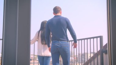 Aşık genç beyaz çiftin arka portresi balkonda kucaklaşıyor ve muhteşem şehir manzarasının tadını çıkarıyor.