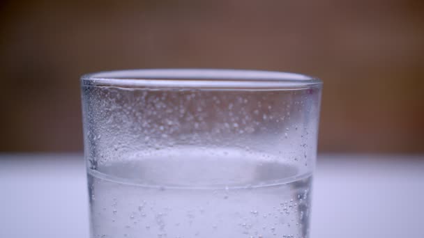 Gros plan macro-pousse d'eau gazeuse pétillante avec des bulles dans un verre transparent debout sur la table blanche — Video