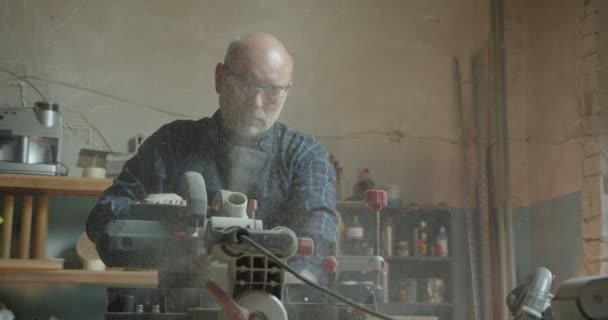 Starší mužský mistr pracující v továrně na dřevo s pilou na řezání dřeva, který je soustředěný a vážný. — Stock video