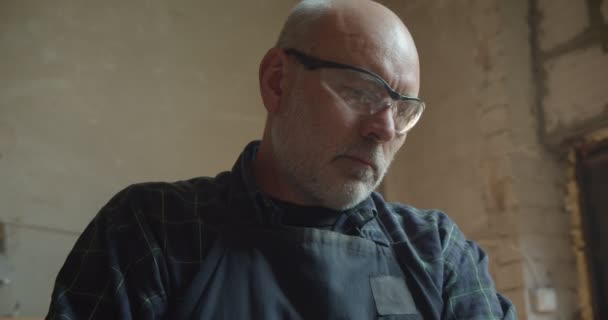 Portret van senior timmerman in beschermende glazen die werkzaam zijn in de productie en geconcentreerd en ernstig zijn. — Stockvideo