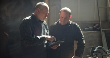 İki marangozluk ustaları tablet izlerken süreci tartışıyor ahşap üretiminde ayakta.