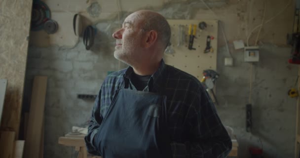 Nahaufnahme Porträt eines Schreinermeisters, der in einer Holzmanufaktur steht und ernst und ruhig in die Kamera schaut. — Stockvideo
