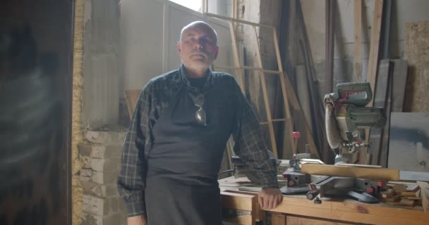 Senior gray haired male professional carpentry master standing at wood manufacture with crossed arms being calm. — Stock Video