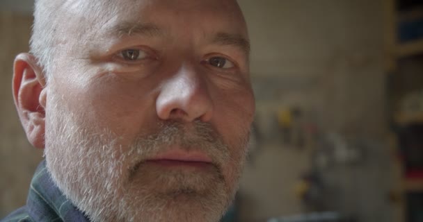 Close-up portret van senior Carpenter bij Wood manufacture kijken naar de camera is ernstig en kalm. — Stockvideo