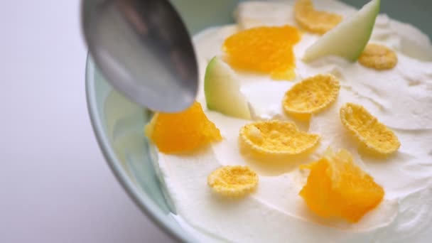 美味酸奶早餐碗的特写镜头，水果和薄片和勺子浸入其中 — 图库视频影像
