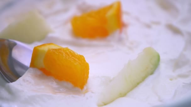 Gros plan macro tige de la main tremper une cuillère dans un bol de yaourt sucré petit déjeuner avec des oranges et des pommes — Video