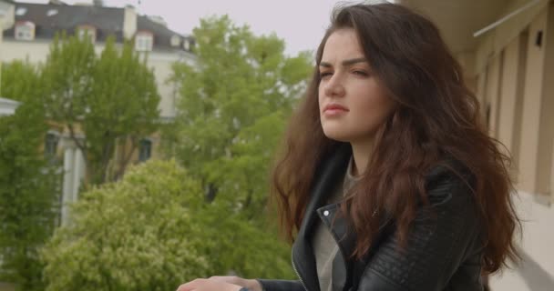Brunette meisje in leren jas op balkon genieten van het spectaculaire uitzicht op de stad horloges in de camera dromerig en verleidelijk. — Stockvideo