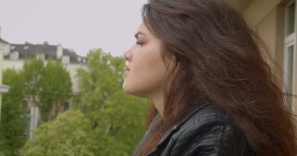 Bruna ragazza in giacca di pelle sul balcone godendo la spettacolare vista sulla città sorride in macchina fotografica essere sognante e seducente . — Video Stock