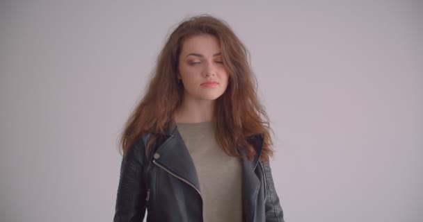 Гарненька брюнетка дівчина в шкіряній куртці дивиться в камеру впевнено ізольована на білому тлі . — стокове відео