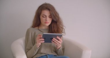 Koltukta tabletle çalışan iş kadını beyaz arka planda izole edilmiş kamerayı sabit olarak izliyor.