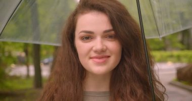 Yeşil şehir parkında kameraya güzel ve sevinçli bir şekilde gülümseyen şemsiyeli kafkas esmer mankeninin yakın çekim çekimi.