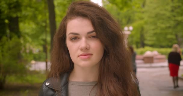 Närbild skott av kaukasiska Brunette kvinnliga klockor i kameran är lugn och glad i den gröna stadsparken. — Stockvideo