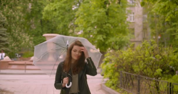 Porträtt av söta kaukasiska brunett kvinna promenader med paraply ler till kameran i den gröna parken. — Stockvideo