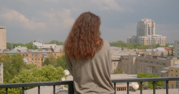 Rear shot van brunette Kaukasisch model op balkon genieten van zonnige urbanistische uitzicht. — Stockvideo