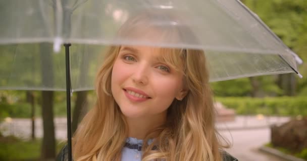 Pretty caucasian blonde student posing happily and seductively with umbrella into camera in the green city park. — Stock Video