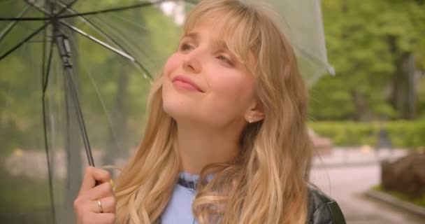 Bella studentessa bionda caucasica in posa gioiosa con ombrello nella fotocamera nel parco verde della città . — Video Stock