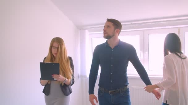 Hembra caucásica agente inmobiliario mostrando y describiendo el apartamento a sus clientes jóvenes caucásicos . — Vídeo de stock