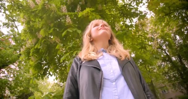 Down top shot of pretty caucasian blonde student standing in the green park observing the beauty of nature. — Stock Video