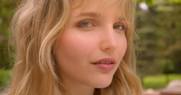 Profil photo de jolie étudiante blonde caucasienne regardant avec sourire dans la caméra dans le parc de la ville verte . — Video