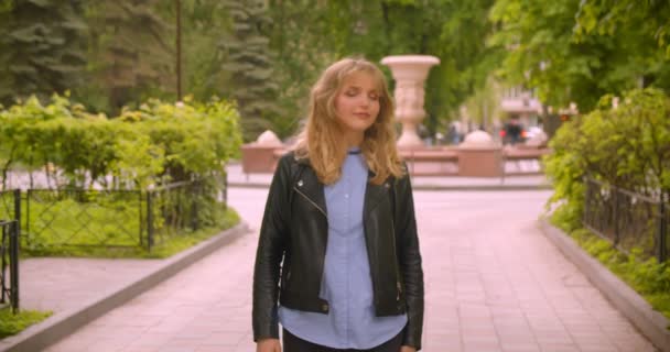 Jolie étudiante blonde caucasienne marchant le long du parc verdoyant observant la beauté de la nature . — Video