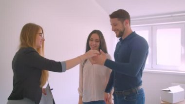 Genç beyaz çift, yeni dairelerinden anahtarları emlakçıdan öpüp sarılmaktan alıyor..