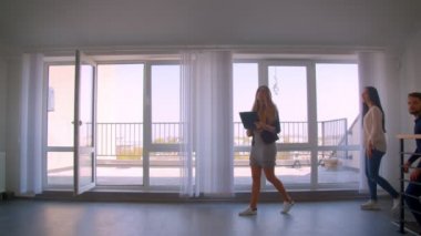 Genç beyaz çifte dairegösteren kadın kafkas emlakçı terasta izlemeye davet ediyor.