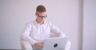 Beyaz bir odada kapalı koltukta oturan dizüstü bilgisayar kullanarak gözlük genç yakışıklı kafkas işadamıcloseup portre