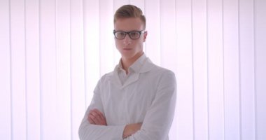 Beyaz bir odada mutlu bir şekilde gülümseyen kameraya bakan gözlüklü genç yakışıklı beyaz işadamının yakın çekim portresi