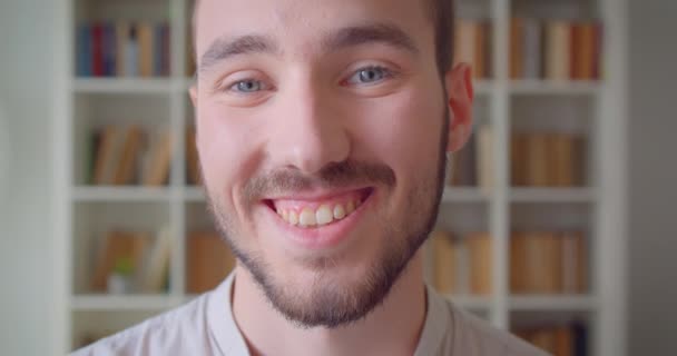 대학 도서관에서 행복하게 미소 짓는 카메라를 보고있는 젊은 잘 생긴 백인 남성 학생의 클로즈업 초상화 — 비디오