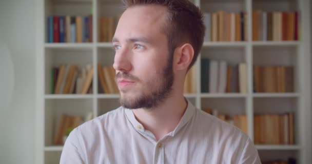 Üniversite kütüphanesinde kameraya bakan genç yakışıklı beyaz erkek öğrencinin yakın çekim portresi — Stok video