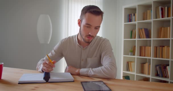 Primer plano retrato de joven guapo caucásico estudiante masculino estudiando y usando la tableta mirando a la cámara sonriendo alegremente en la biblioteca de la universidad — Vídeo de stock