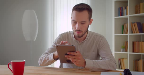 Retrato de cerca del joven hombre de negocios caucásico guapo usando la tableta en el interior del apartamento — Vídeos de Stock