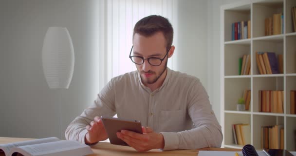 Closeup portrét mladého krásného kavkazského obchodníka v brýlích s tabletovým interiérem v bytě — Stock video