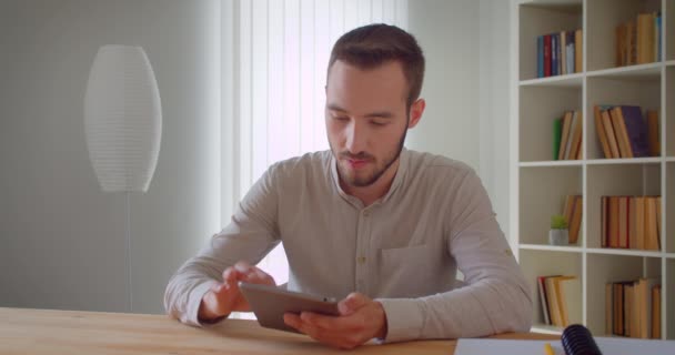 Nahaufnahme Porträt eines jungen gutaussehenden kaukasischen Geschäftsmannes, der mit dem Tablet in die Kamera in der Wohnung schaut — Stockvideo