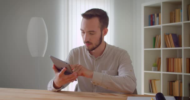 Κοντινό πορτραίτο του νεαρού όμορφου καυκάσιου επιχειρηματία που χρησιμοποιεί το tablet και δείχνει την οθόνη του πράσινου κλειδιού στην κάμερα σε εσωτερικούς χώρους στο διαμέρισμα με ράφια στο παρασκήνιο — Αρχείο Βίντεο