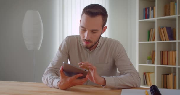 Closeup portré fiatal csinos kaukázusi üzletember használja a tablettát, és bemutatja a zöld chroma képernyő kamera zárt a lakásban a könyvespolcok a háttérben — Stock videók