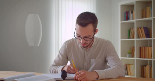 Üniversite kütüphanesinde kameraya bakarak tableti inceleyen ve kullanan gözlüklü genç yakışıklı beyaz erkek öğrencinin yakın çekim portresi — Stok video