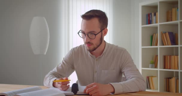 Üniversite kütüphanesinde tablet ilerleyen ve kullanan gözlüklü genç ve yakışıklı beyaz erkek öğrencinin yakın çekim portresi — Stok video