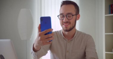 Genç yakışıklı beyaz işadamının telefonda selfie çekerken yakın çekim portresi evde ki dizüstü bilgisayarın önünde mutlu bir şekilde otururken