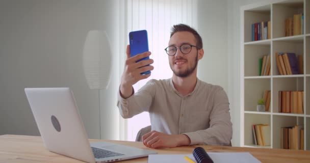 Primer plano retrato de jóvenes guapos caucásicos de negocios selfies en el teléfono sentado delante de la computadora portátil en el interior del apartamento en el interior — Vídeos de Stock