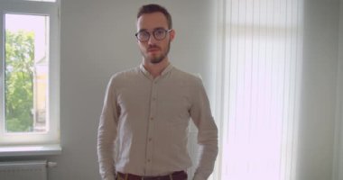 Genç yakışıklı beyaz işadamının gözlüklü yakın çekim portresi dairenin iç mekanına kamerayla bakıyor