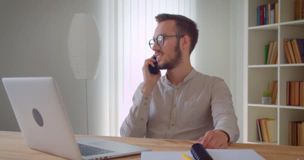 Zbliżenie portret młodego przystojnego kaukaski biznesmen o telefon siedzi przed laptopem w pomieszczeniu w mieszkaniu — Wideo stockowe