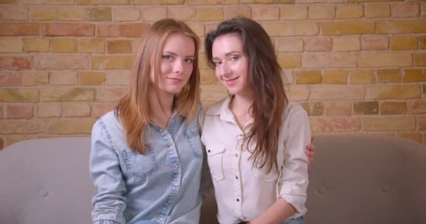 Съемки крупным планом молодой красивой лесбийской пары, смотрящей на камеру, сидящую на диване в недавно купленной квартире — стоковое видео