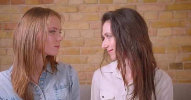 Nahaufnahme eines jungen schönen lesbischen verliebten Paares, das glücklich lächelnd in die Kamera auf der Couch in einer neu gekauften Wohnung sitzt — Stockvideo