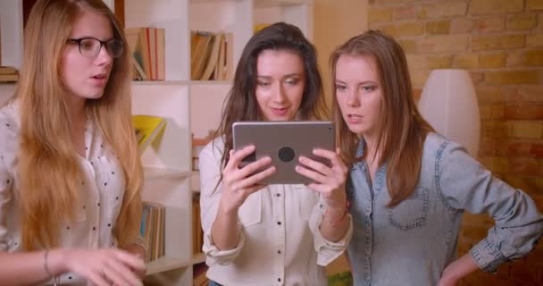 Closeup shoot of young beautiful lesbian couple talking to female realtor about purchasing an apartment using the touchscreen indoors — Stock Video