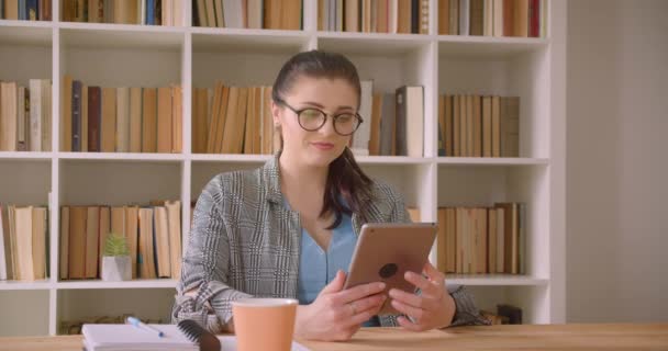 Nahaufnahme einer jungen kaukasischen Geschäftsfrau, die das Tablet benutzt und der Kamera im Bibliotheksbüro grünen Bildschirm zeigt — Stockvideo